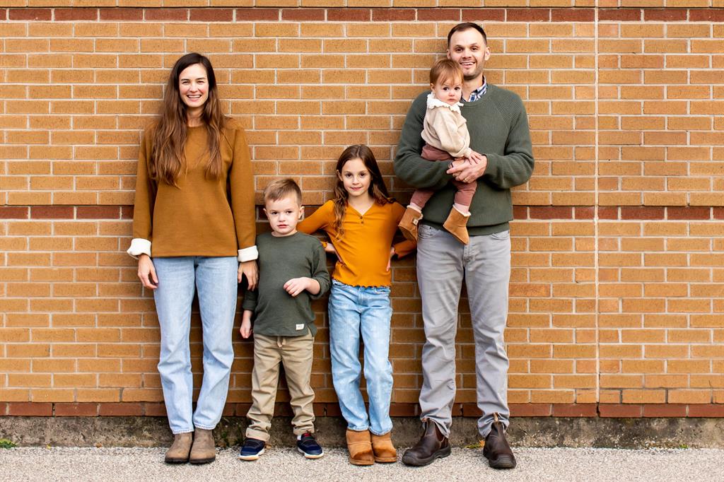 A family of five stand against a brick wall